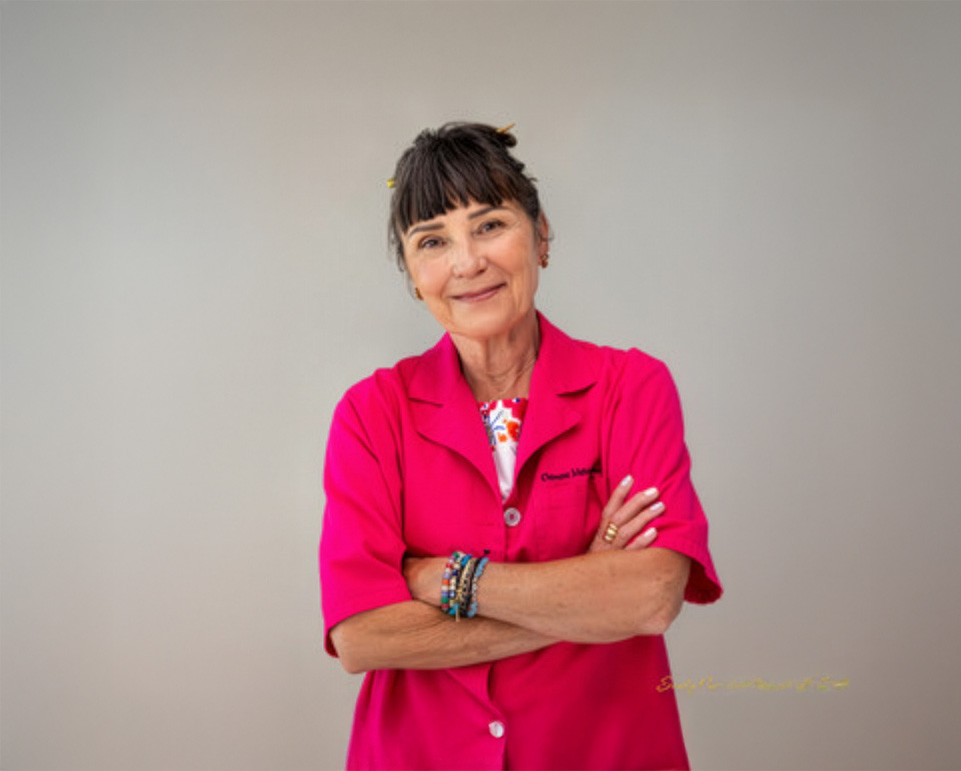 Dr.Lucas stands with her arms crossed and warm smile, wearing a bright pink shirt.